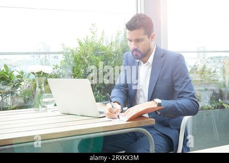 Businessman writing in notebook with laptop in restaurant Stock Photo