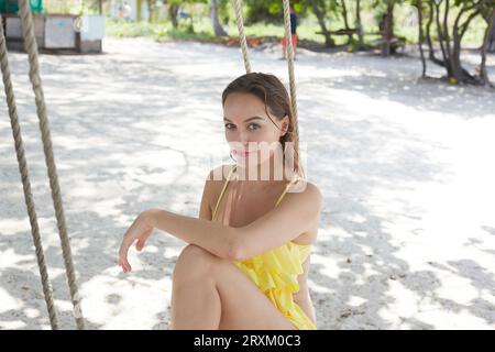 Young woman wearing yellow on beach swing Stock Photo