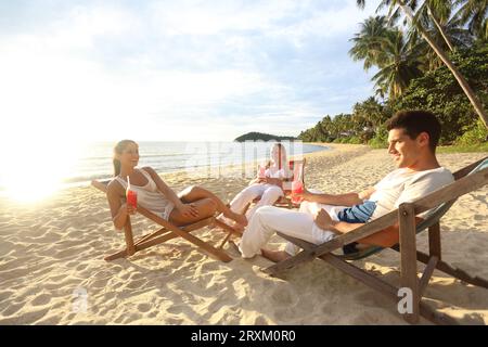 Young people sitting on deck chairs on beach Stock Photo
