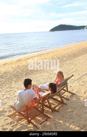 Young people sitting on deck chairs on beach Stock Photo