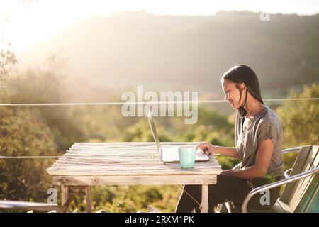 Young woman using laptop on balcony at sunset Stock Photo
