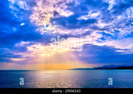Beautiful seascape with colorful clouds and bright sun rays cast over calm sea waters and hazy distant shores. Sunrise or sunset in Mediterranean sea, soft focus background.  Stock Photo