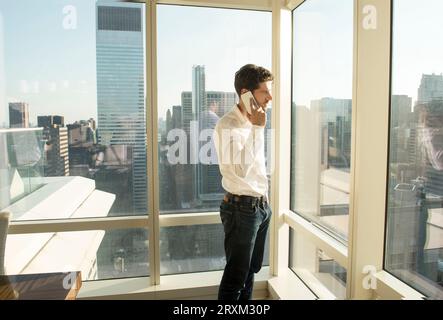 Young man using smartphone by window in New York City Stock Photo