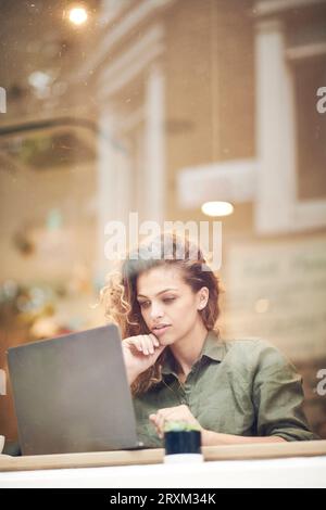 Young woman using laptop behind cafe window Stock Photo