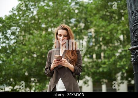 Mid adult woman smiling while texting on smart phone Stock Photo