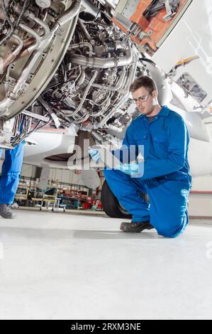 Crouched man using digital table by airplane Stock Photo
