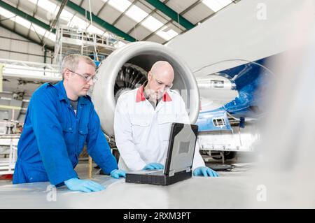 Men using laptop by airplane in hangar Stock Photo