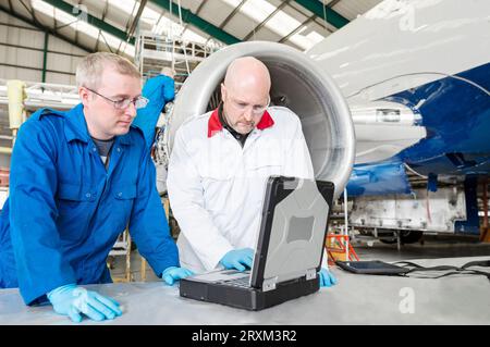 Men using laptop by airplane in hangar Stock Photo