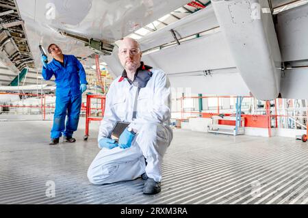 Man holding digital tablet crouched underneath airplane Stock Photo