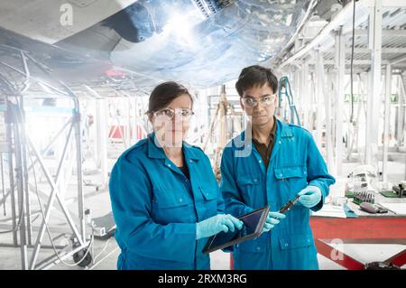 Workers using digital tablet by airplane in hangar Stock Photo