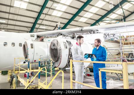 Men using digital tablet in airplane hangar Stock Photo