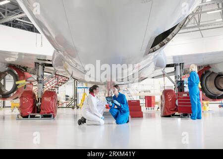Crouched women using digital tablet under airplane Stock Photo