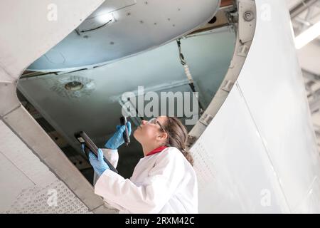 Female worker using torch in airplane doorway Stock Photo
