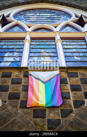 Pride flag hanging below a stained glass window on the front of a church in downtown Portland Oregon Stock Photo