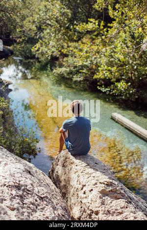 Man sitting on rock above river Stock Photo