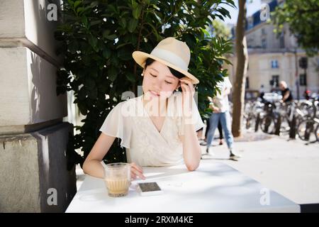 Woman wearing straw hat using smart phone at table Stock Photo