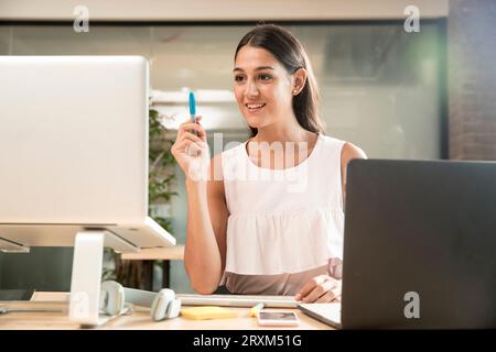 Young woman holding pen by laptop Stock Photo