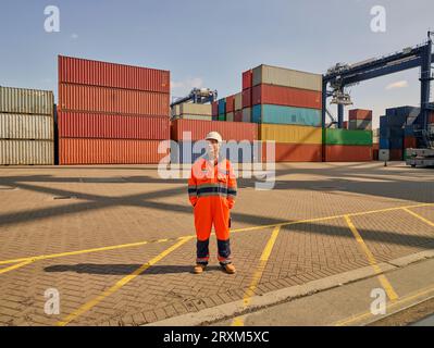 Dock worker in reflective overalls by cargo containers Stock Photo