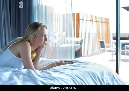 Woman lying on a bed gazing outside Stock Photo