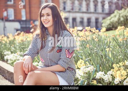 Delighted teen girl sitting in meadow and drawing in sketchbook