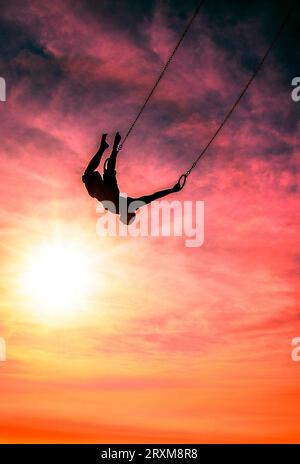 Silhouette of man swinging on gymnastic rings during sunset Stock Photo