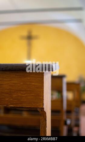 Dark brown church pews with light yellow background of altar and crucifix Stock Photo