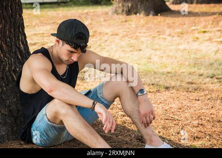 A man sitting against a tree in a park, tired, sad or depressed, thinking with his head down Stock Photo