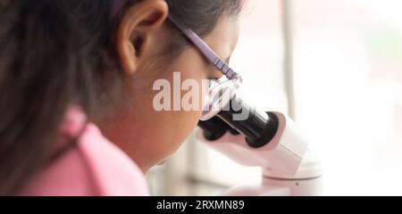 Children scientist learning on biology and chemistry in the laboratory. A STEM education learning concept. An Asian student girl using microscope in a Stock Photo