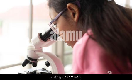 Children scientist learning on biology and chemistry in the laboratory. A STEM education learning concept. An Asian student girl using microscope in a Stock Photo