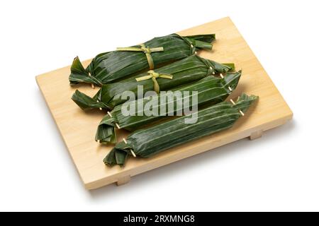 Fresh homemade Lemper wrapped in banana leaves, an Indonesian savoury snack made of glutinous rice  close up at a bamboo board isolated on white backg Stock Photo