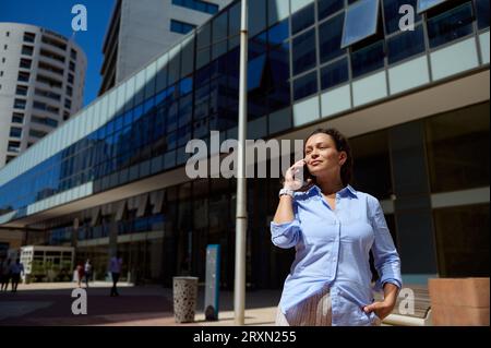 Authentic professional confident portrait, multi-ethnic beautiful woman entrepreneur freelancer communicating online, talking on smartphone against mo Stock Photo