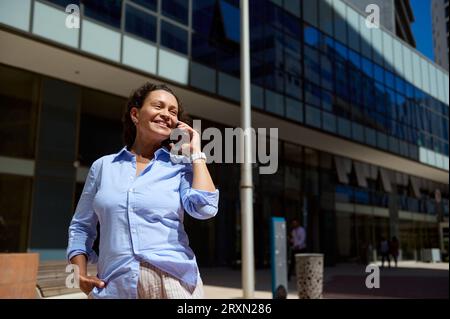 Confident authentic professional portrait of a middle aged multi-ethnic purposeful businesswoman, entrepreneur talking on her smart mobile phone Stock Photo