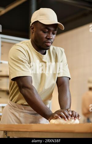 Vertical portrait of young Black man as baker kneading dough in artisan bakery Stock Photo