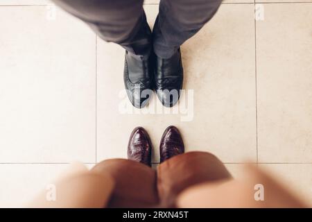 Top view of couple's shoes. Man wearing black leather classic chelsea woman wears burgundy crocodile boots. Close up Stock Photo