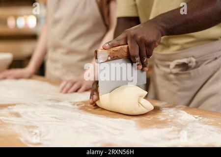 Close up of unrecognizable Black man cutting dough for fresh bread in bakery, copy space Stock Photo