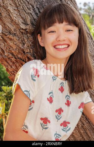 11 year old laughing girl leaning against a tree Stock Photo
