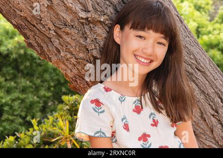 Eleven year old smiling girl leaning against a tree Stock Photo