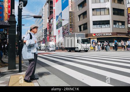 An elderly Japanese man stands beside a pedestrian crossing in Ikebukuro, Tokyo, Japan Stock Photo