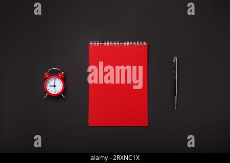 Black background red alarm clock notepad pen blank space desktop. Top view Stock Photo