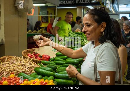 A woman buys garlic at a vegetable stall at the indoor Montrouge Sunday market in the suburbs of Paris, France. Stock Photo