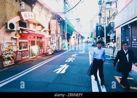 Two men walk past a restaurant beneath a railway line in Shimbashi, Tokyo, Japan Stock Photo