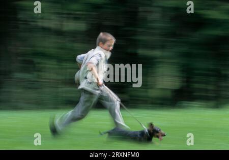 Little boy running fast to his little one with dog, motion focus 8, 9, 10, 11 years old - Stock Photo