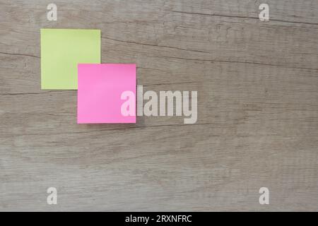 Two paper square sticky notes in yellow and pink colors on a wooden background Stock Photo