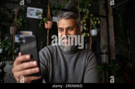 Office work, senior businessman looking at the phone screen while sitting at the table and smiling Stock Photo