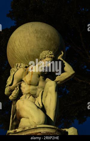 Classical statue of Atlas carrying globe in Portmeirion village gardens at dusk Stock Photo