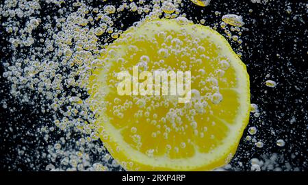 Underwater of freshly squeezed sweetened lemonade which raw lemons slice falling in soda water against dark blue or black background. Close up lemonad Stock Photo