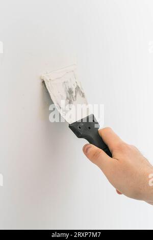 Male using spatula and plastering of wall with white fresh finishing putty. Closeup. Repair work of home. Side view. Stock Photo