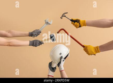 Female and male hands holding different construction tools and safety hardhat on beige background Stock Photo