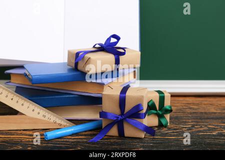 Gift boxes with books and different stationery on brown wooden table in classroom Stock Photo