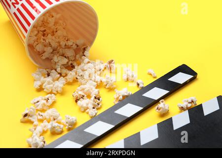 Bucket with tasty popcorn and clapperboard on yellow background Stock Photo